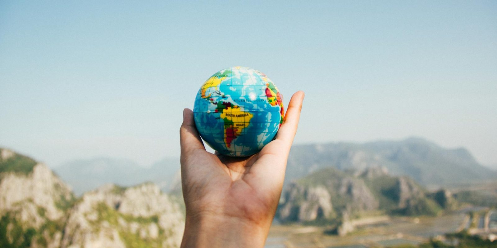 person holding world globe facing mountain